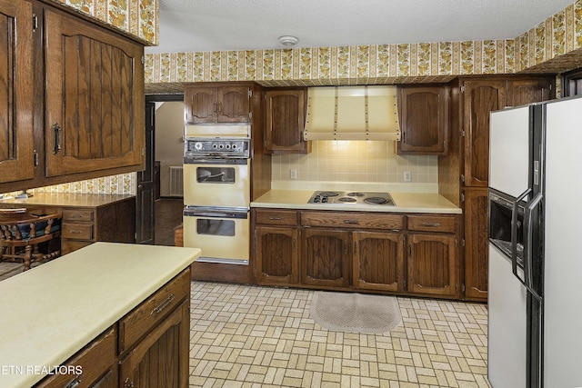 kitchen featuring multiple ovens, wallpapered walls, light countertops, electric cooktop, and white fridge with ice dispenser