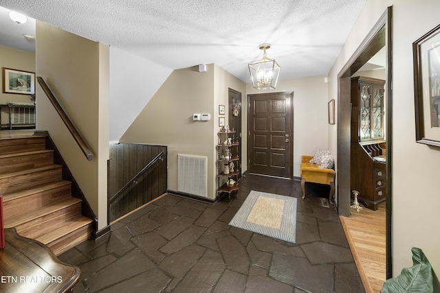 foyer featuring visible vents, stairs, dark wood-type flooring, a textured ceiling, and a chandelier