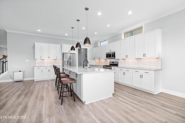 kitchen featuring a breakfast bar area, a sink, stainless steel appliances, light wood-style floors, and crown molding