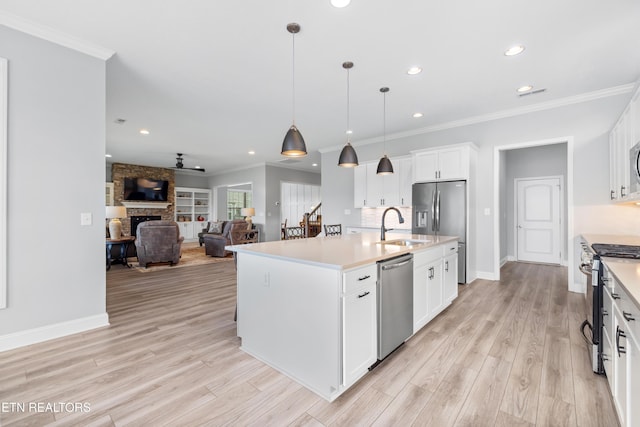 kitchen with crown molding, open floor plan, light wood-type flooring, a stone fireplace, and stainless steel appliances