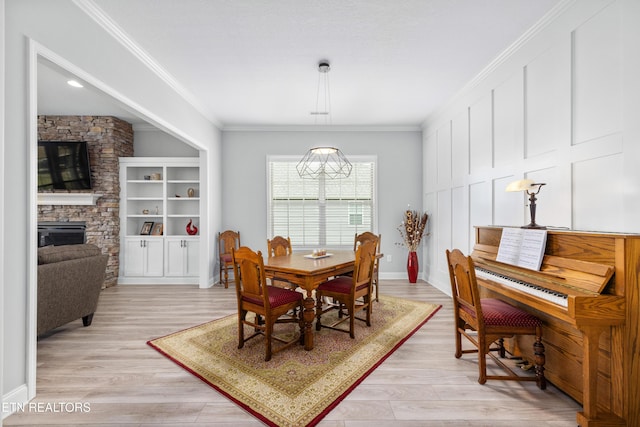 dining area featuring light wood-type flooring, ornamental molding, and a fireplace