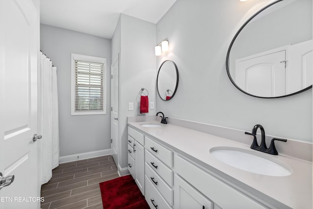 bathroom with double vanity, wood finish floors, baseboards, and a sink