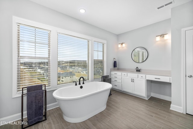 bathroom with visible vents, baseboards, wood finish floors, a freestanding bath, and vanity