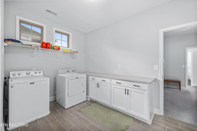 washroom featuring visible vents, baseboards, wood tiled floor, washer and clothes dryer, and cabinet space