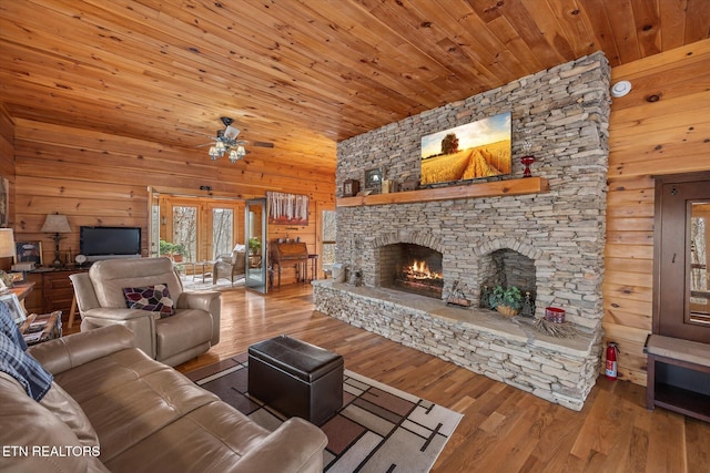 living area featuring a stone fireplace, wood walls, wood ceiling, and wood finished floors