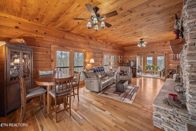 dining area featuring wood walls, light wood-style flooring, french doors, wooden ceiling, and a ceiling fan