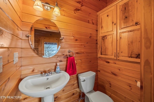 bathroom featuring wood walls, toilet, and a sink