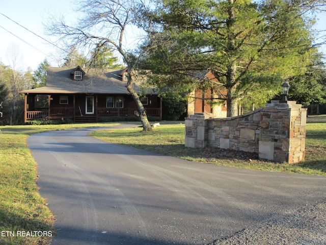 view of front of property with aphalt driveway, covered porch, and a front yard