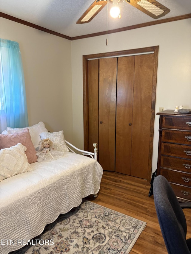 bedroom with crown molding, ceiling fan, wood finished floors, a closet, and a textured ceiling