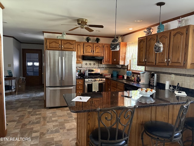 kitchen featuring ornamental molding, under cabinet range hood, tasteful backsplash, appliances with stainless steel finishes, and a peninsula