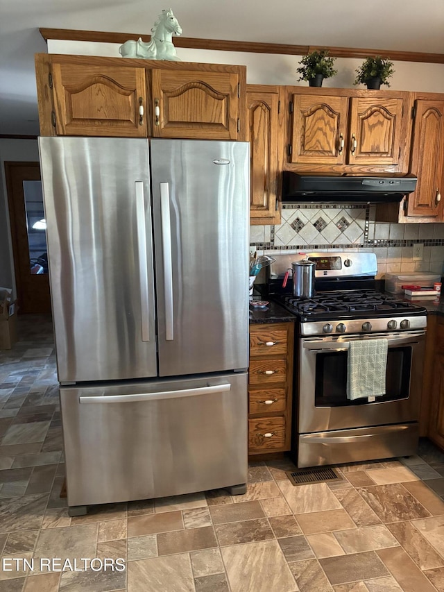 kitchen featuring dark countertops, stone finish flooring, under cabinet range hood, decorative backsplash, and stainless steel appliances