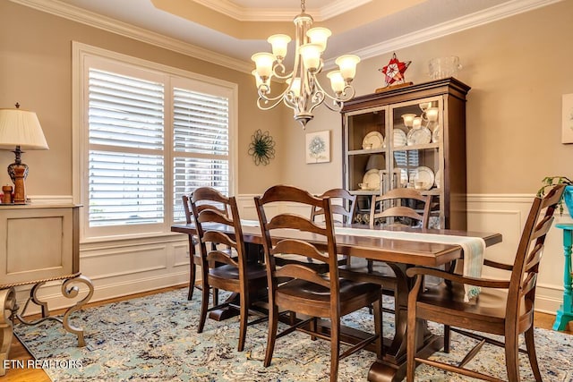 dining room featuring wood finished floors, a tray ceiling, ornamental molding, wainscoting, and a chandelier