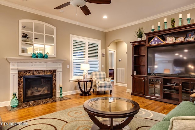 living room featuring visible vents, crown molding, a premium fireplace, wood finished floors, and arched walkways