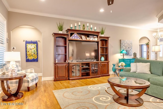 living area featuring a notable chandelier, light wood-style flooring, ornamental molding, arched walkways, and baseboards