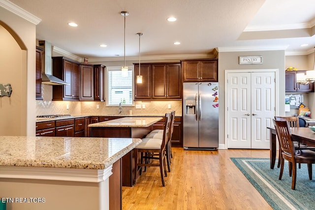 kitchen featuring a sink, stainless steel appliances, dark brown cabinets, wall chimney range hood, and a center island