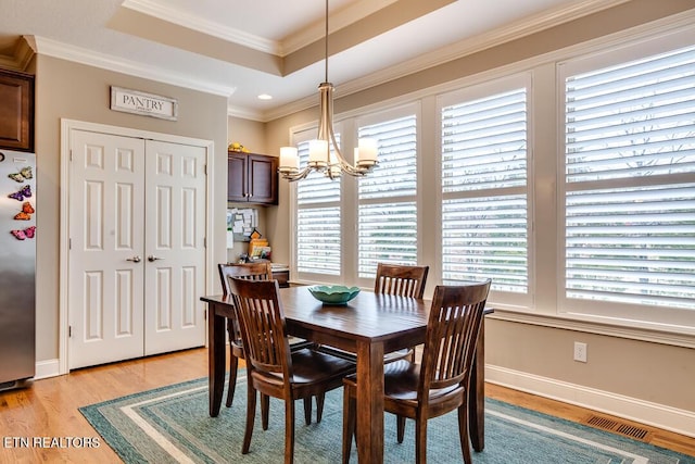 dining space featuring visible vents, crown molding, a tray ceiling, light wood-style floors, and an inviting chandelier