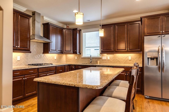 kitchen with a center island, wall chimney range hood, light stone countertops, light wood-style floors, and stainless steel appliances