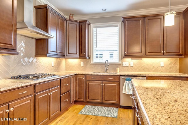 kitchen featuring crown molding, light wood-type flooring, appliances with stainless steel finishes, wall chimney exhaust hood, and a sink