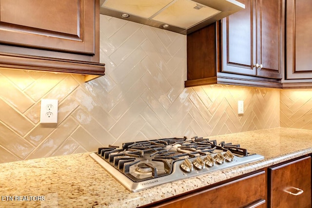 kitchen featuring light stone counters, tasteful backsplash, stainless steel gas stovetop, and under cabinet range hood