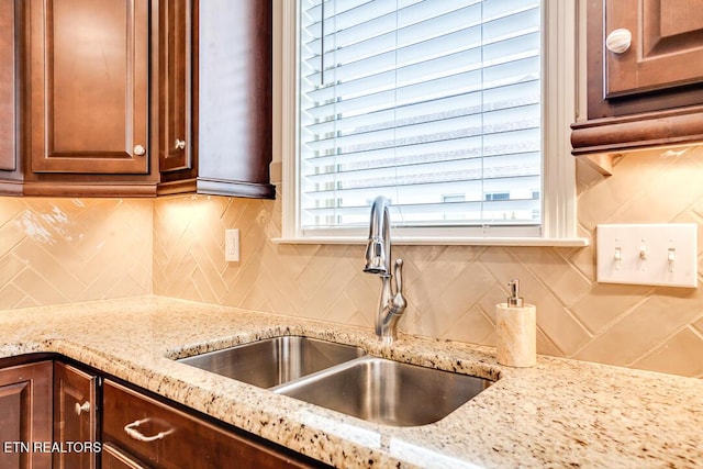 kitchen featuring decorative backsplash, dark brown cabinets, light stone countertops, and a sink