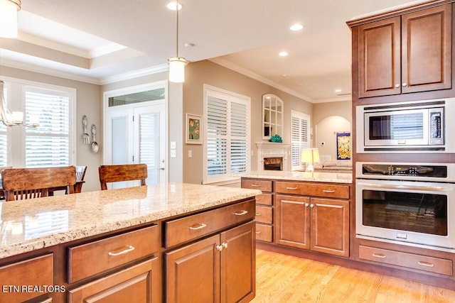 kitchen featuring brown cabinetry, light stone countertops, light wood finished floors, stainless steel appliances, and crown molding