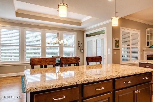 kitchen with a chandelier, wood finished floors, a raised ceiling, and ornamental molding