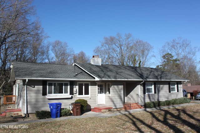 ranch-style house with a shingled roof, a front yard, and a chimney