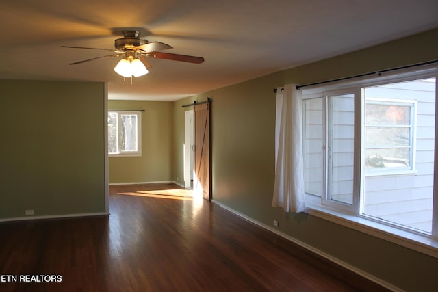 empty room featuring ceiling fan, baseboards, a barn door, and dark wood-style flooring