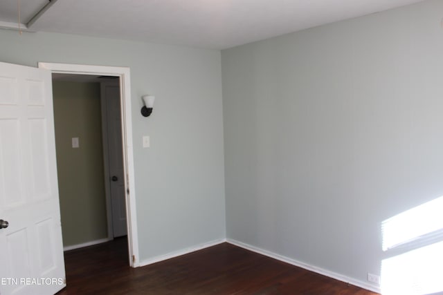 empty room featuring dark wood finished floors, attic access, and baseboards