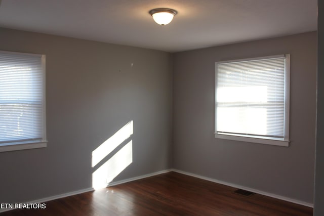 empty room with dark wood-style floors, baseboards, and visible vents