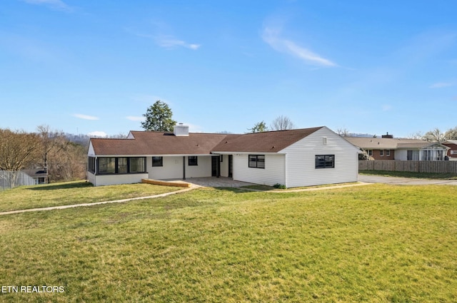 view of front of house with a patio, fence, a front yard, a sunroom, and a chimney