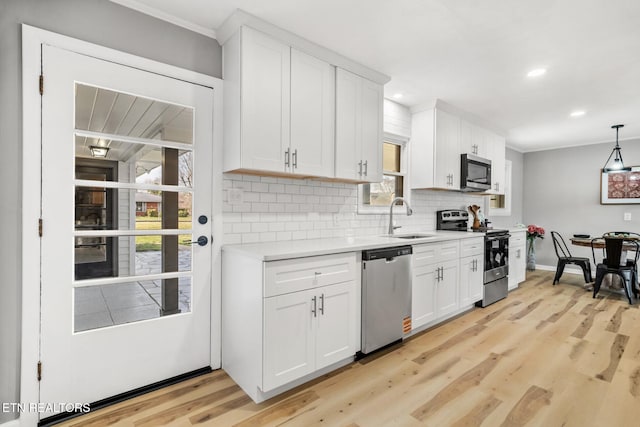 kitchen featuring light wood finished floors, light countertops, decorative backsplash, stainless steel appliances, and a sink