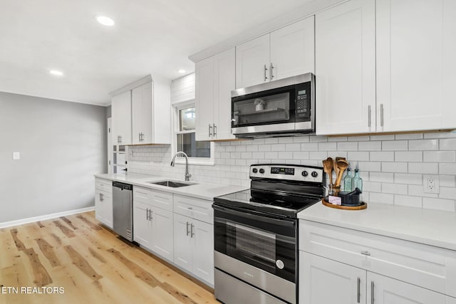 kitchen with backsplash, light countertops, light wood-style flooring, appliances with stainless steel finishes, and a sink