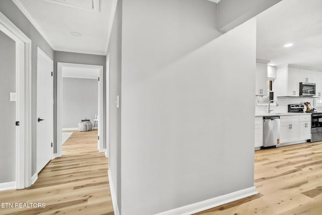 hallway with baseboards, light wood finished floors, and a sink