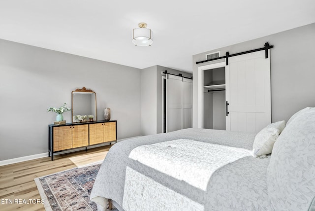 bedroom with visible vents, wood finished floors, a barn door, a closet, and baseboards