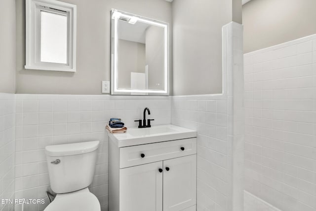 bathroom featuring a wainscoted wall, vanity, toilet, and tile walls