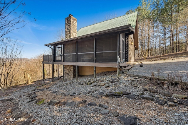 back of house with metal roof, a chimney, and a sunroom