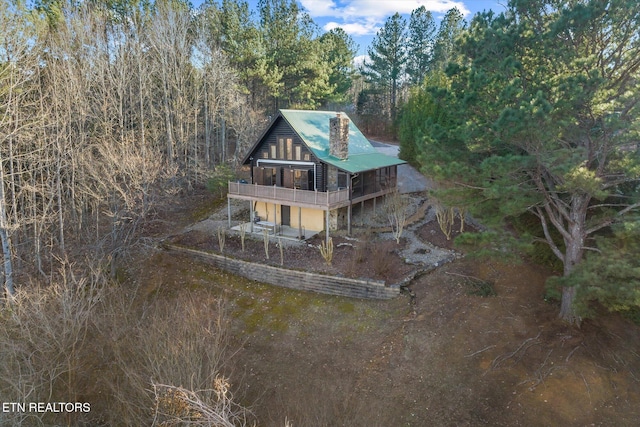 rear view of house with dirt driveway, a wooded view, and a chimney