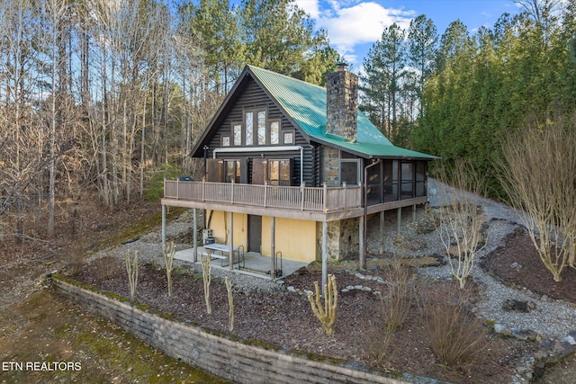 back of house featuring stone siding, a patio, a wooden deck, metal roof, and a chimney