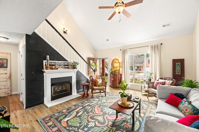 living area featuring stairway, wood finished floors, visible vents, a fireplace with flush hearth, and vaulted ceiling