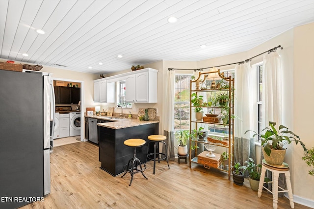 kitchen featuring white cabinetry, freestanding refrigerator, a peninsula, a breakfast bar area, and light wood finished floors