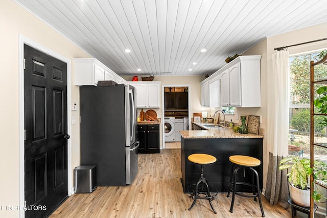 kitchen featuring a peninsula, freestanding refrigerator, washer / clothes dryer, white cabinetry, and a sink