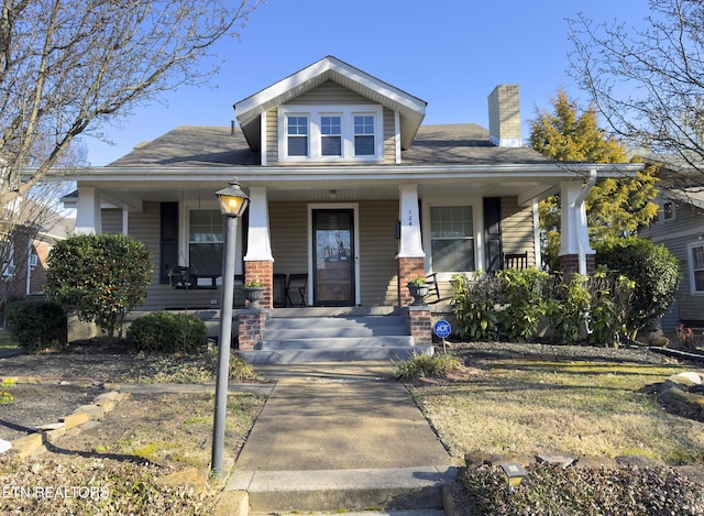 view of front of property featuring brick siding, a porch, and a chimney