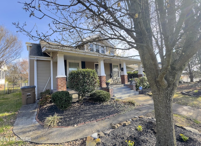 view of front of property featuring brick siding, covered porch, and fence