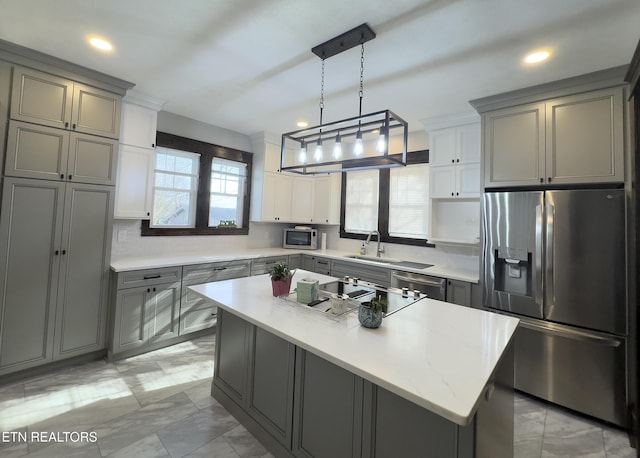 kitchen featuring gray cabinetry, a center island, decorative light fixtures, appliances with stainless steel finishes, and a sink