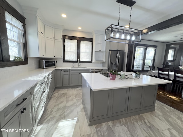 kitchen with a kitchen island, light countertops, gray cabinets, appliances with stainless steel finishes, and a sink