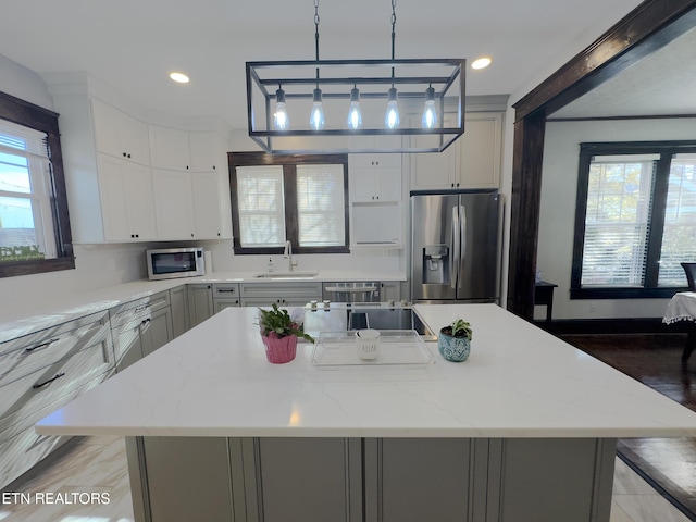 kitchen featuring a sink, stainless steel appliances, a wealth of natural light, and decorative light fixtures