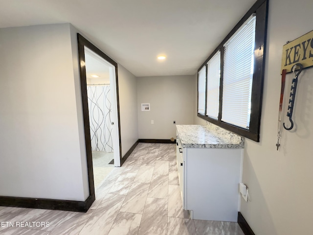 interior space featuring baseboards, white cabinets, and light stone countertops