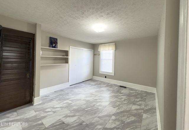 unfurnished bedroom with visible vents, baseboards, a textured ceiling, and a closet