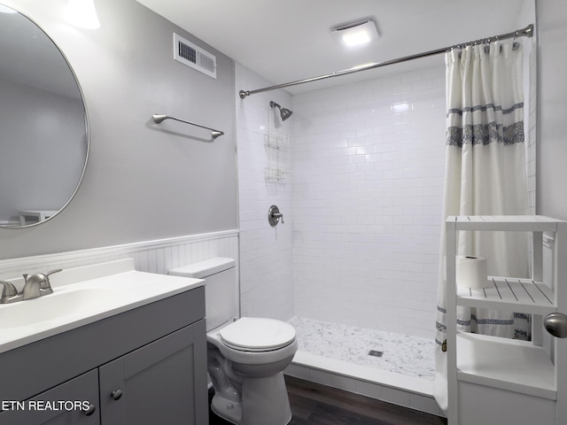 bathroom featuring visible vents, toilet, a tile shower, wainscoting, and wood finished floors